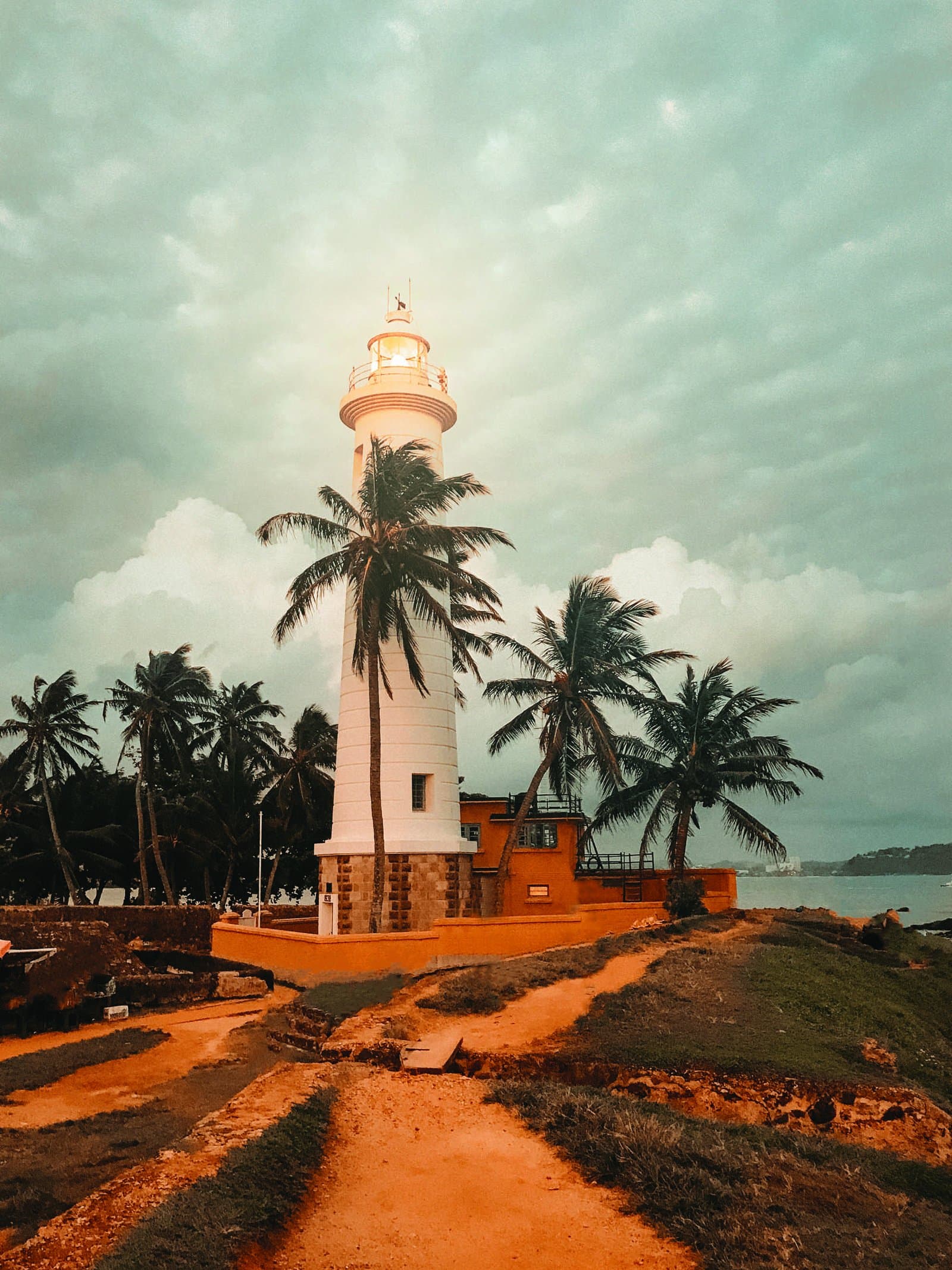 Galle Fort lighthouse among palm trees at sunset