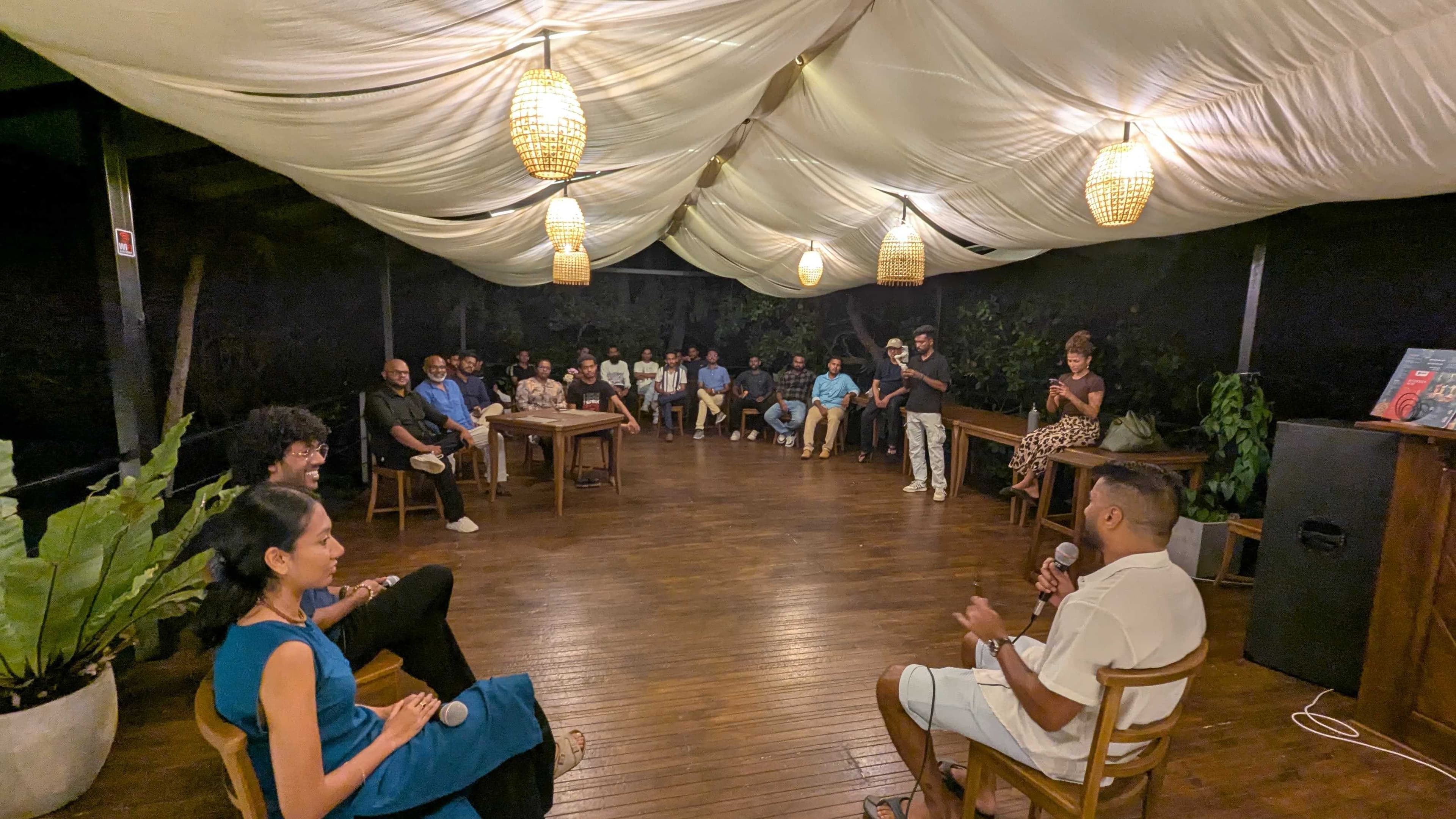 A founder fireside chat on a wooden deck, speaker with microphone facing a seated circle